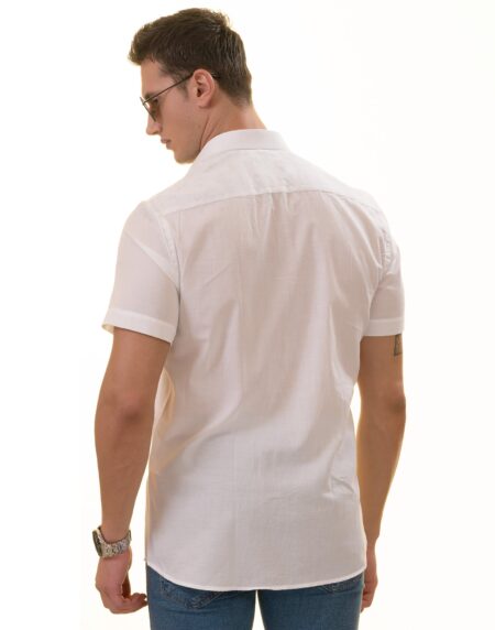 A man wearing a white paisley short sleeve shirt with a spread collar, paired with a red hat and sunglasses, standing against a white background.